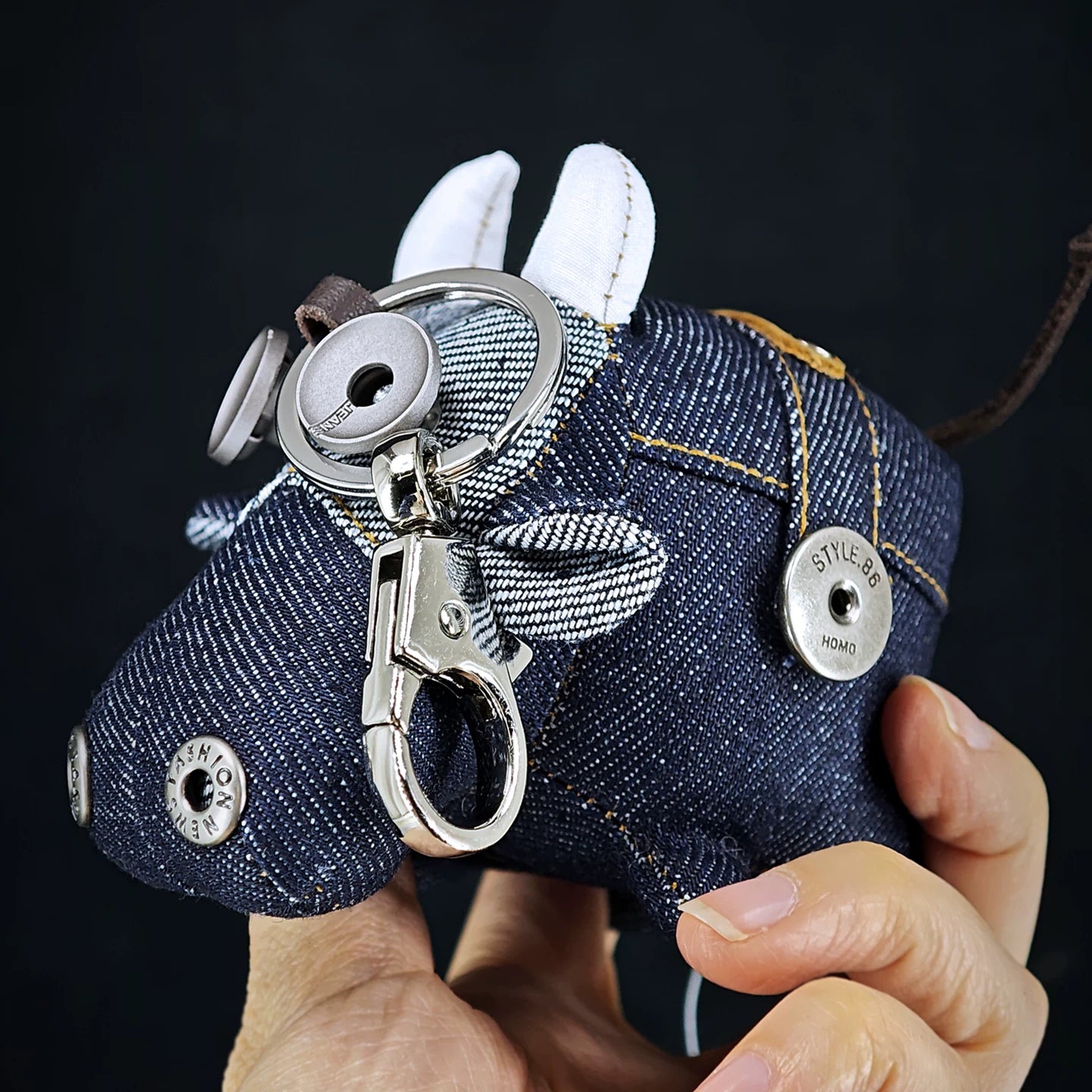 Indigo ox figurine with tan leather tag and weathered metal hardware. Dark rustic artisan craft, macabre folk art keychain.