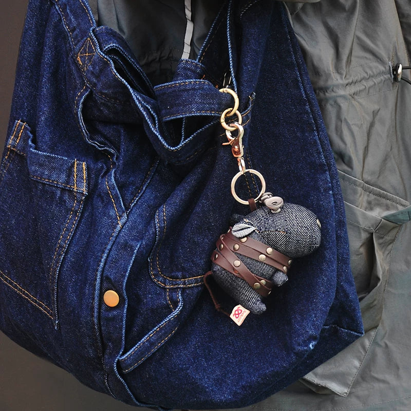 Denim hippo keychain showing visible twill texture and weathered metal hardware. Dark artisan craft, macabre folk art toy.