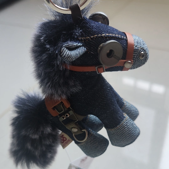 Denim horse showing textural weave and weathered metal buckles. Dark aesthetic artisan craft, macabre folk art piece.