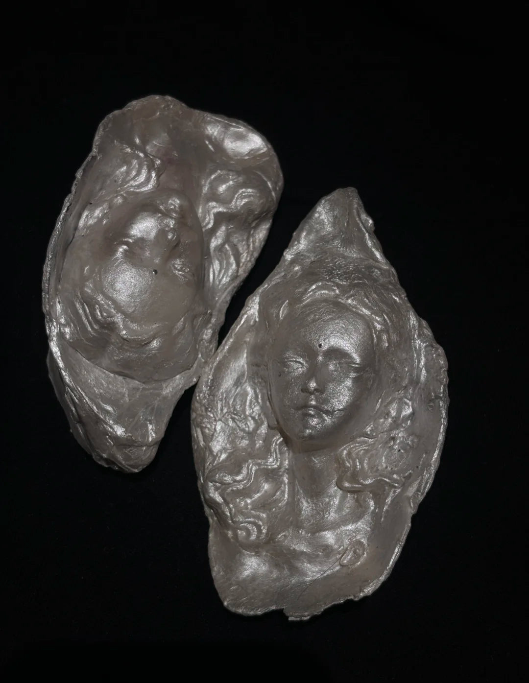 Three sculptural silver-toned baroque pearl pendant reliefs showing three different facial expressions—curly hair, closed eyes, and open eyes—arranged in a triangular composition against a black background