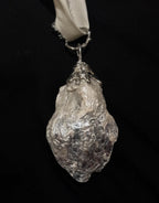 A silver metallic sculptural relief of a woman's face with closed eyes, curly flowing hair, and an irregular organic base, displayed against a solid black background