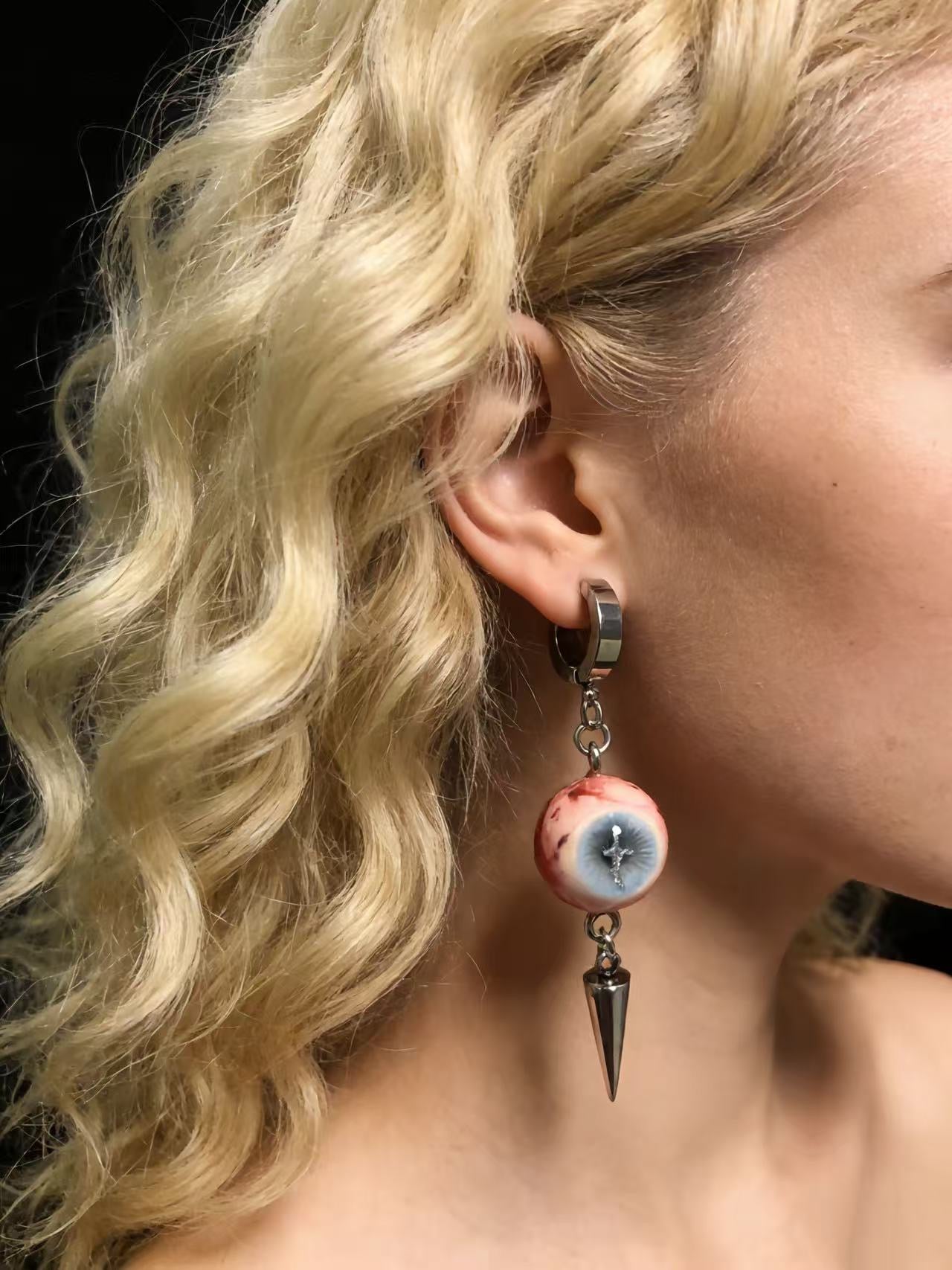 Side profile of model wearing cross eyeball earrings highlighting dramatic movement and metallic shine
