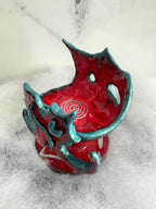 Red glazed alien ceramic vessel with teal trim, white spiral interior pattern, on white fluffy faux fur, marble