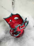 Red and teal glazed alien ceramic vessel, grotesque organic shape, on white fluffy faux fur, marble background