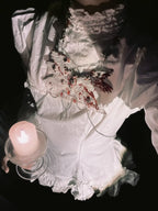 Angel cage body chain on white gothic dress, person holds lit candle, shadowy dark background