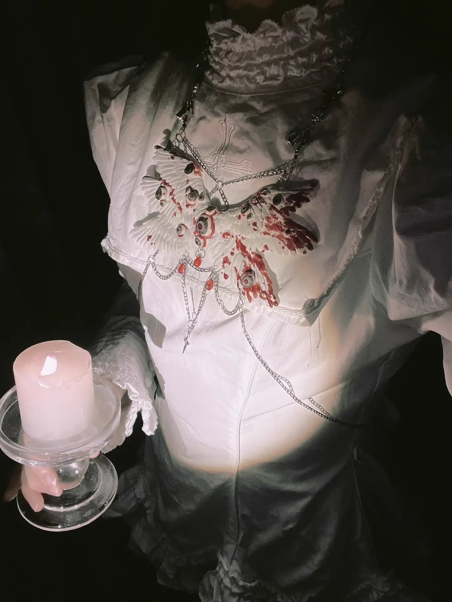 Angel cage wing body chain on white gothic dress, person holds lit candle, moody low dark lighting