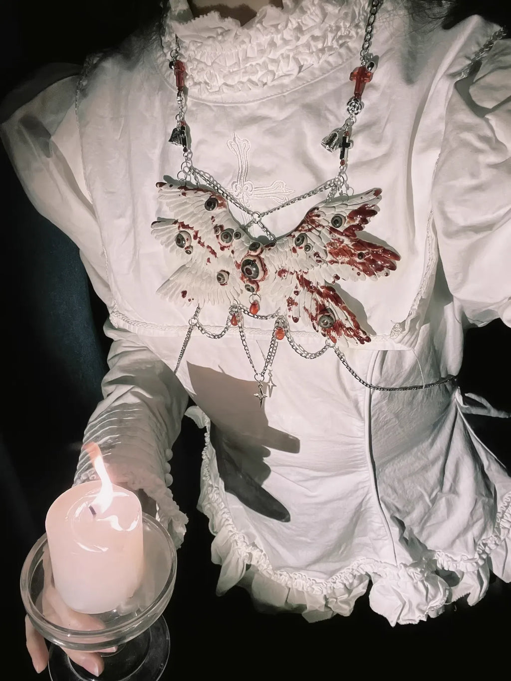 Angel cage body chain worn on white ruffled gothic dress, person holds lit candle in glass, dark background