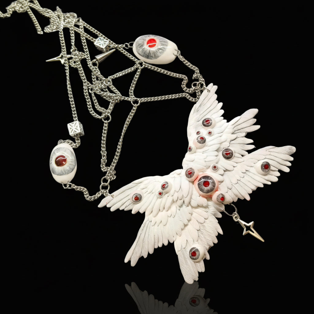Gothic ceramic angel wing body chain relic laid flat on dark surface — white sculpted feather panels studded with red glass eyeballs, silver multi-strand chains, spiked terminals, cube-form charm, and star pendants arranged in full display. The eyeballs do not close.