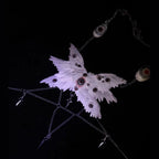  Gothic ceramic angel wing body chain relic suspended against pure black — six sculpted white feather panels spread wide, each surface embedded with glass eyeballs of varying diameter. Silver multi-strand chains descend from the lower edge. The wings do not fold. They have never folded.