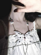 Relic ceramic angel wing body chain in high-contrast monochrome rendering — white feather panels bleached to near-white against deep black ground, glass eyeball inlays visible as dark voids within the wing surface. The chain is a thin silver thread. The form is absolute.