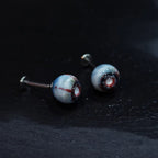 Pair of glossy resin bloodshot necrotic eyeball cartilage studs on dark textured background