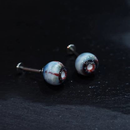 Pair of glossy resin bloodshot necrotic eyeball cartilage studs on dark textured background