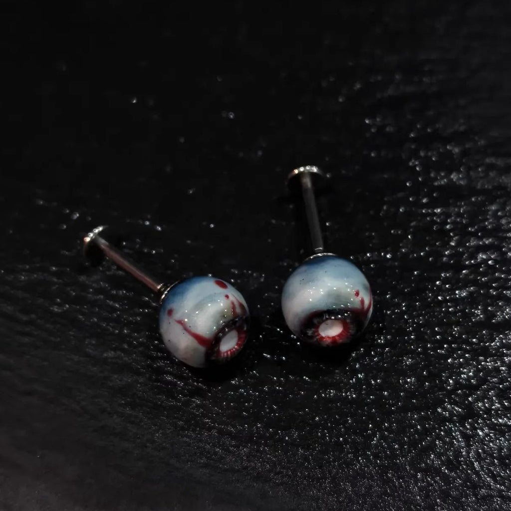 Pair of glossy resin bloodshot necrotic eyeball cartilage studs on solid black background