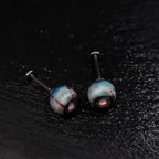 Pair of glossy resin bloodshot necrotic eyeball cartilage studs on solid black background