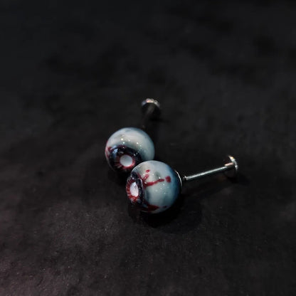 Side view of pair of cinnabar necrotic eyeball cartilage studs on dark sparkly black background
