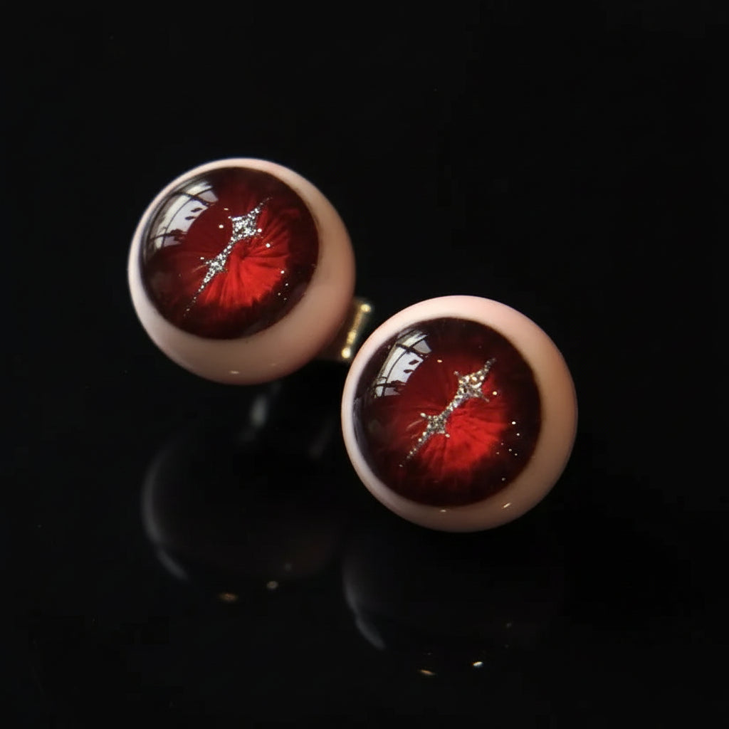 Pair of crimson magma slit pupil eyeball cartilage studs on black reflective background