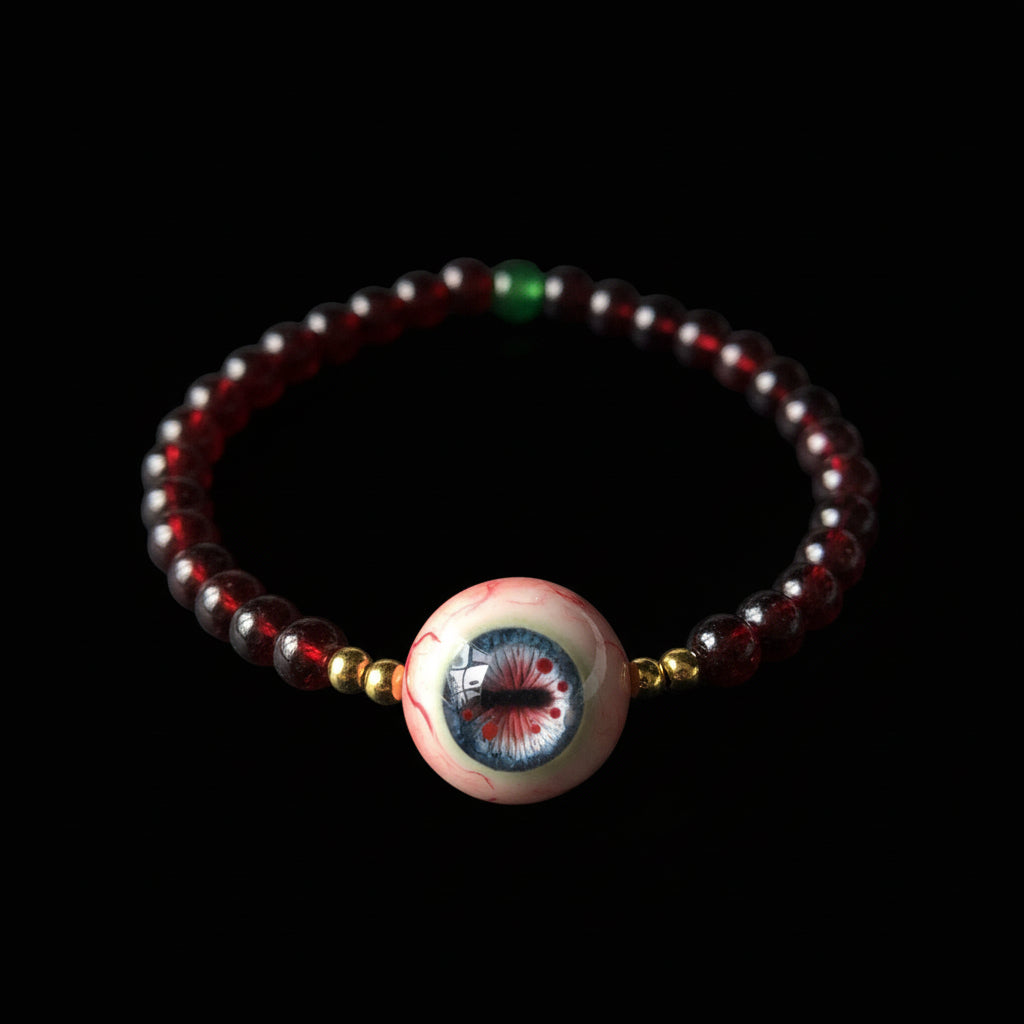 Single strand Cthulhu eyeball bracelet, deep red garnet beads, green accent, gold spacers, focal eyeball on black