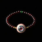 Single strand Cthulhu eyeball bracelet, deep red garnet beads, green accent, gold spacers, focal eyeball on black