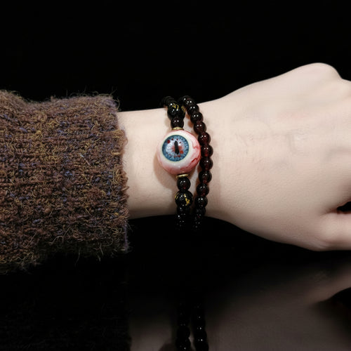 Double wrap Cthulhu eyeball bracelet worn on wrist with fuzzy brown sweater cuff on black