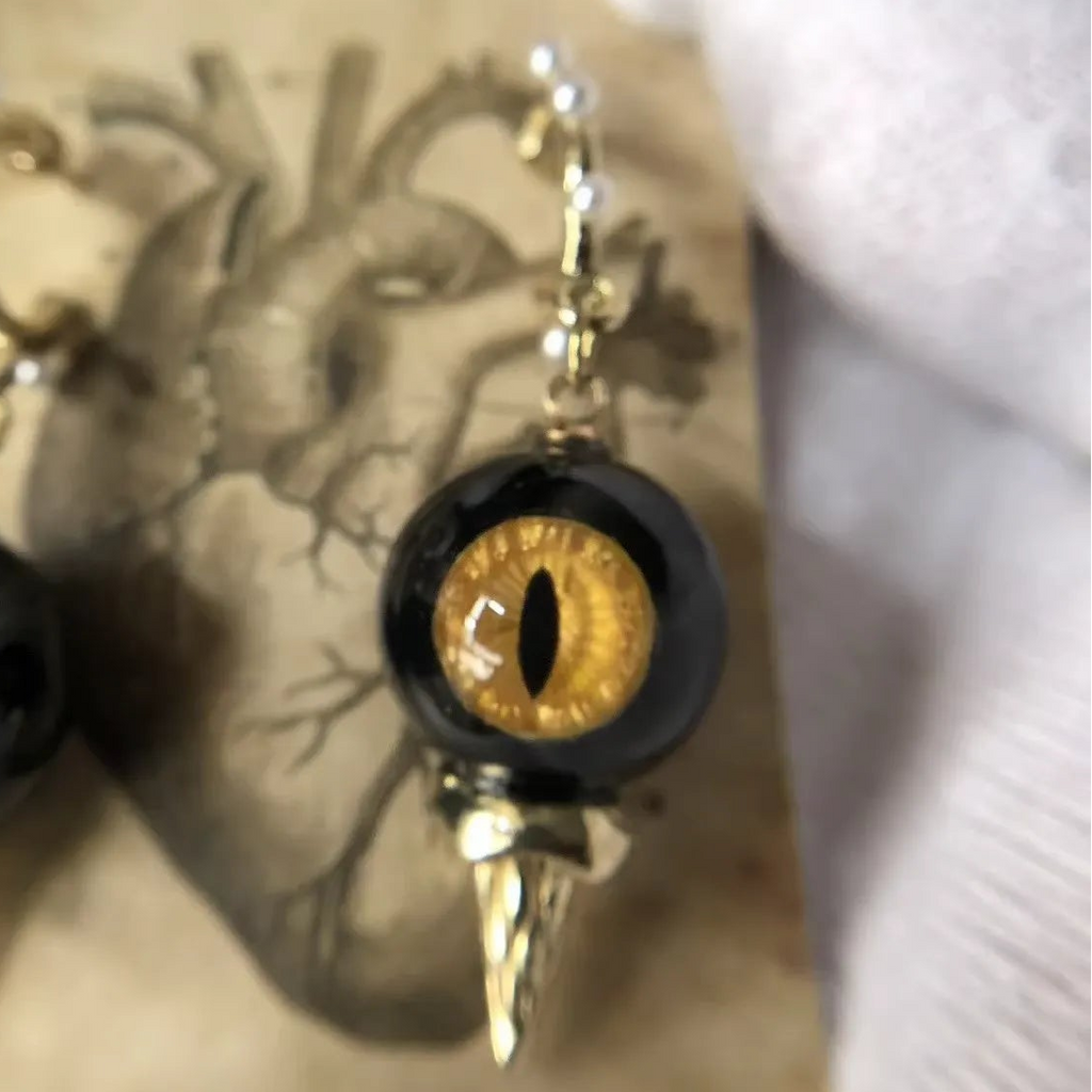 Close-up of single obsidian feline cat eye abyssal spike drop earring on vintage printed paper