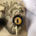 Close-up of single obsidian feline cat eye abyssal spike drop earring on vintage printed paper