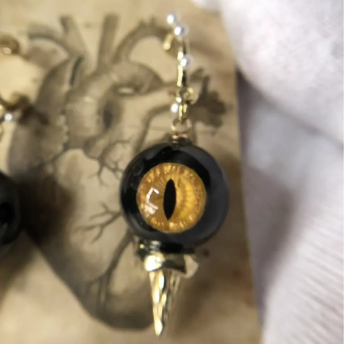 Close-up of single obsidian feline cat eye abyssal spike drop earring on vintage printed paper