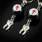 Close-up of gothic crimson cross faux eyeball tooth charm drop earrings on black background