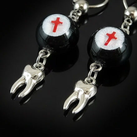 Close-up of gothic crimson cross faux eyeball tooth charm drop earrings on black background