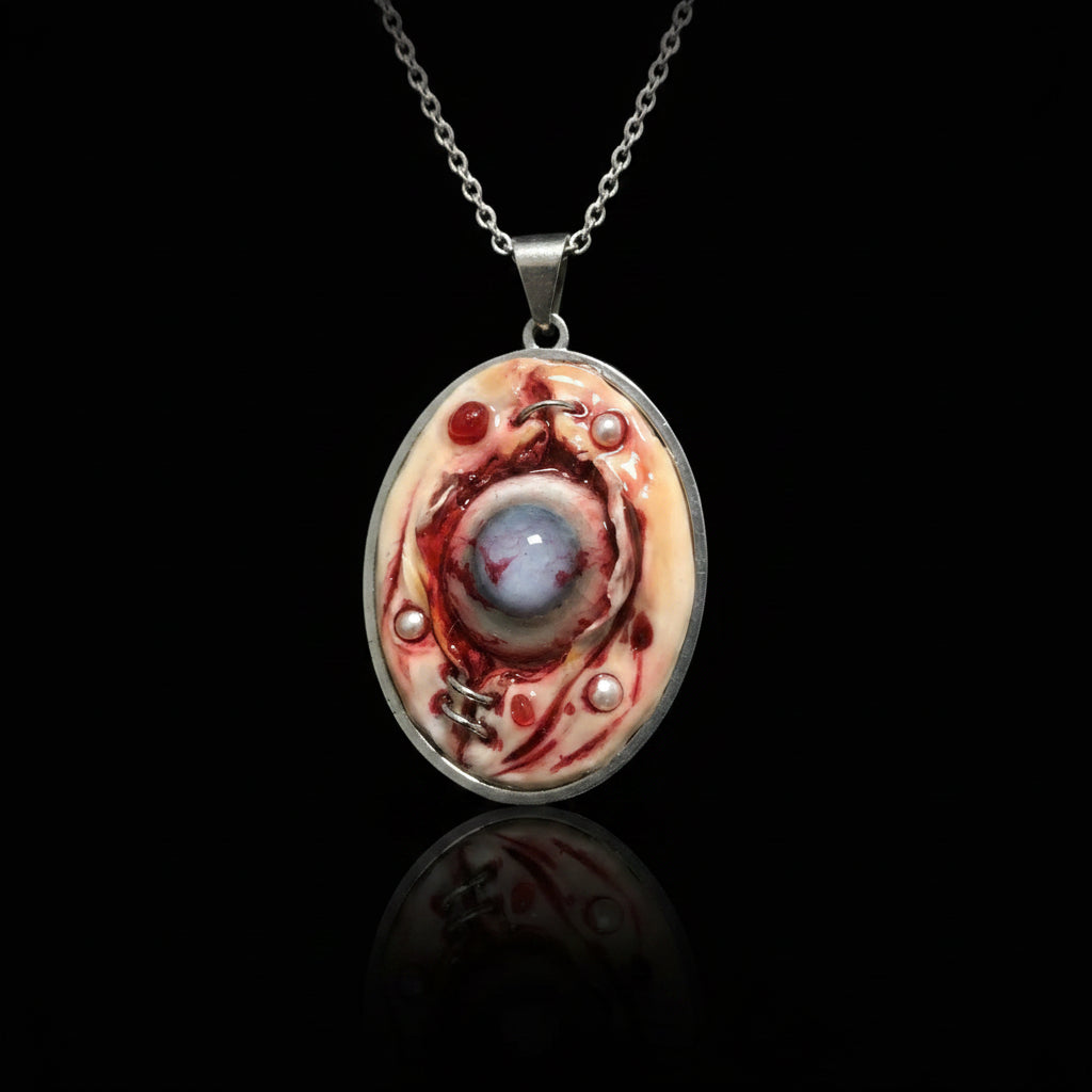 Front view of oval silver bezel pendant with raw flesh texture, embedded eyeball, pearl and red beads on black