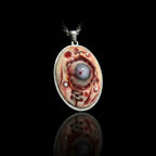 Front view of oval silver bezel pendant with raw marbled flesh texture, red veining and central glass eye detail on black