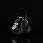A black leather kiss-lock frame purse with three surreal oyster shell eye embellishments featuring blue irises, pink eyelids, and white eyelashes, silver spherical charms, and a twisted black leather handle against a white fabric background