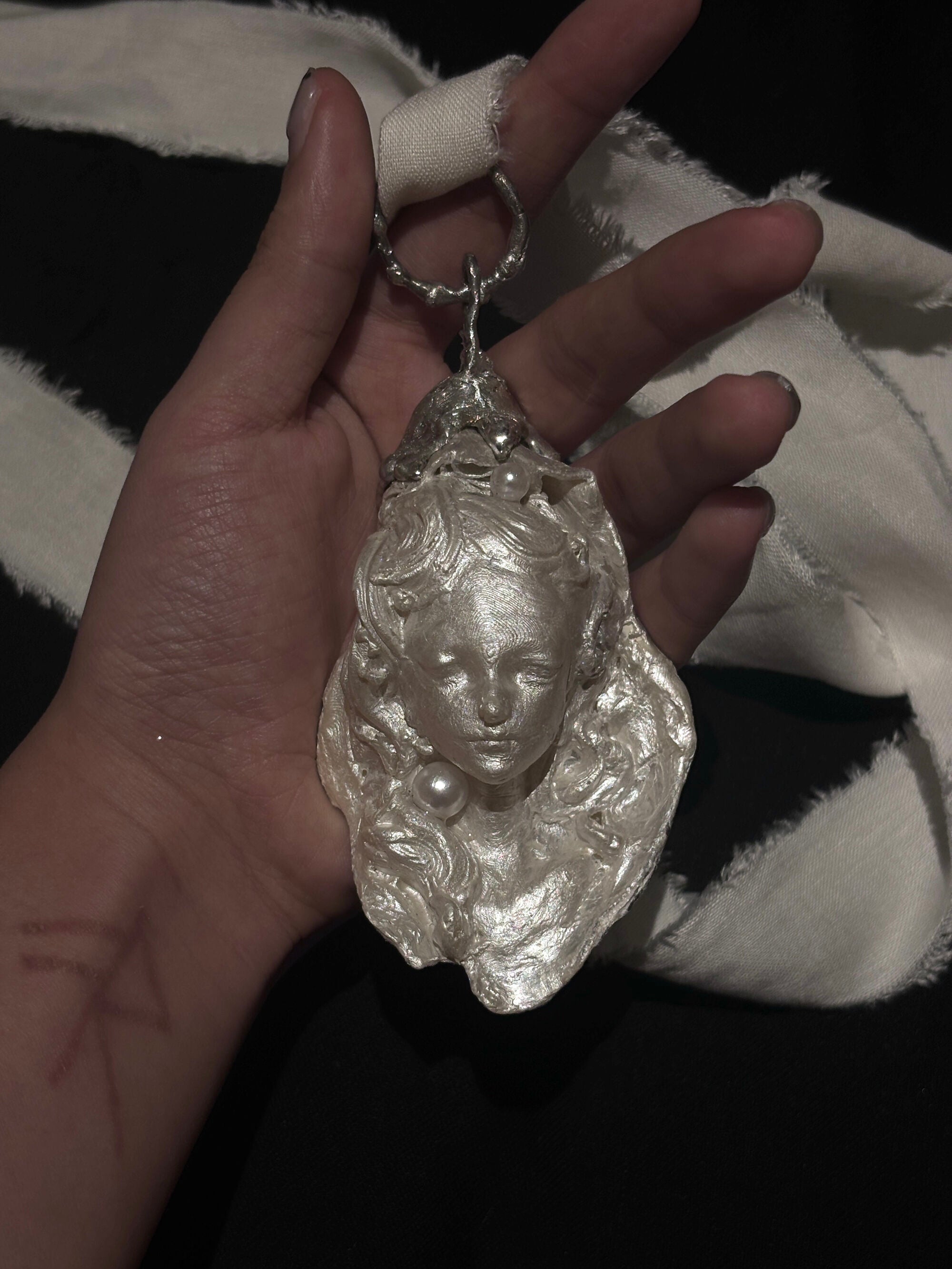 Two sculptural silver-toned baroque pearl pendant casts showing contrasting facial expressions, displayed side by side against a solid black background